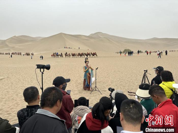圖為2023年4月底，敦煌大漠“逐舞者”奧楠在鳴沙山月牙泉景區(qū)視頻直播，吸引游人圍觀?！●T志軍 攝